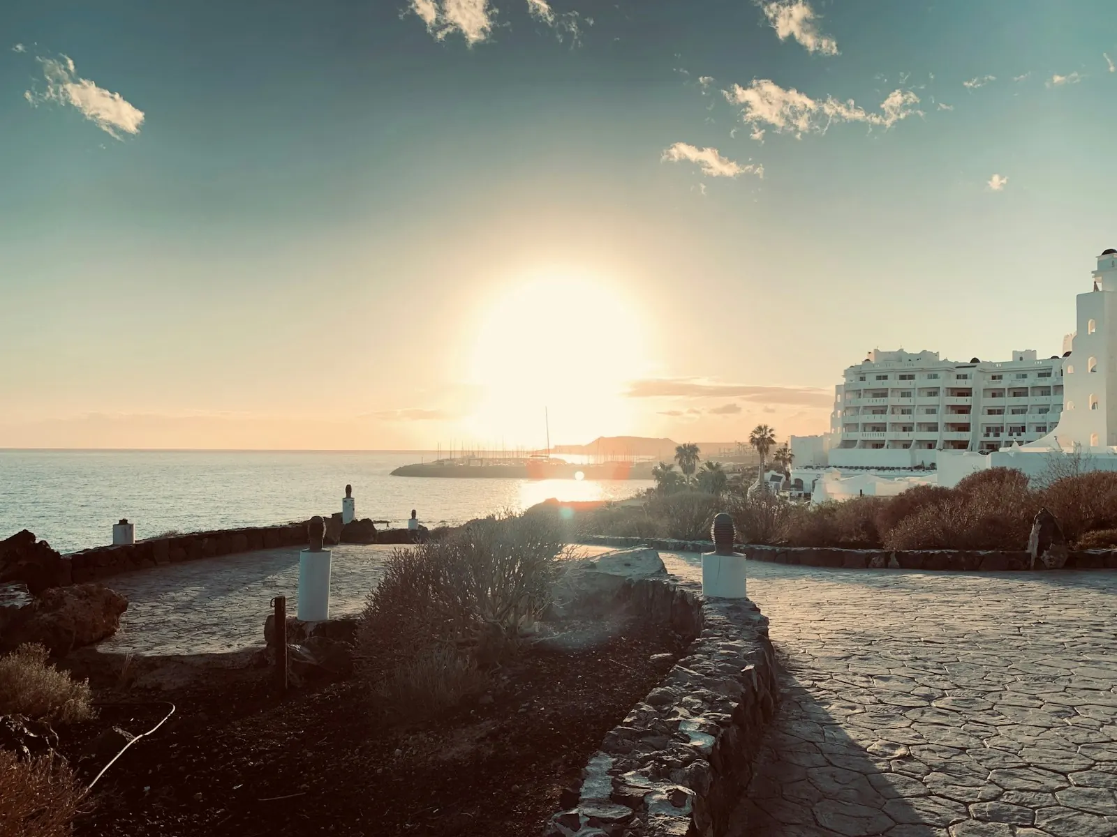 Seafront path in Golf del Sur at sunset, with white apartment buildings and the marina in the distance