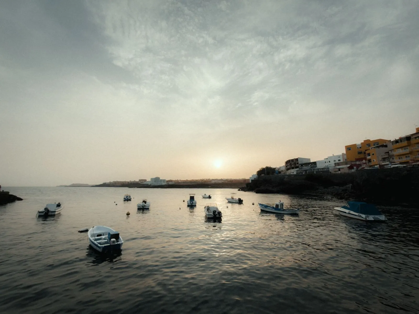 Petits bateaux amarrés dans le port de Los Abrigos au coucher du soleil, avec des maisons colorées face à la mer