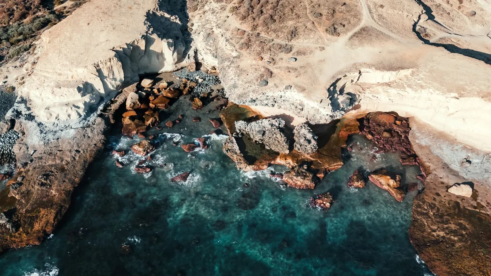 Aerial view of the rocky coast at La Caleta, Tenerife, with pale cliffs, boulders and clear turquoise water