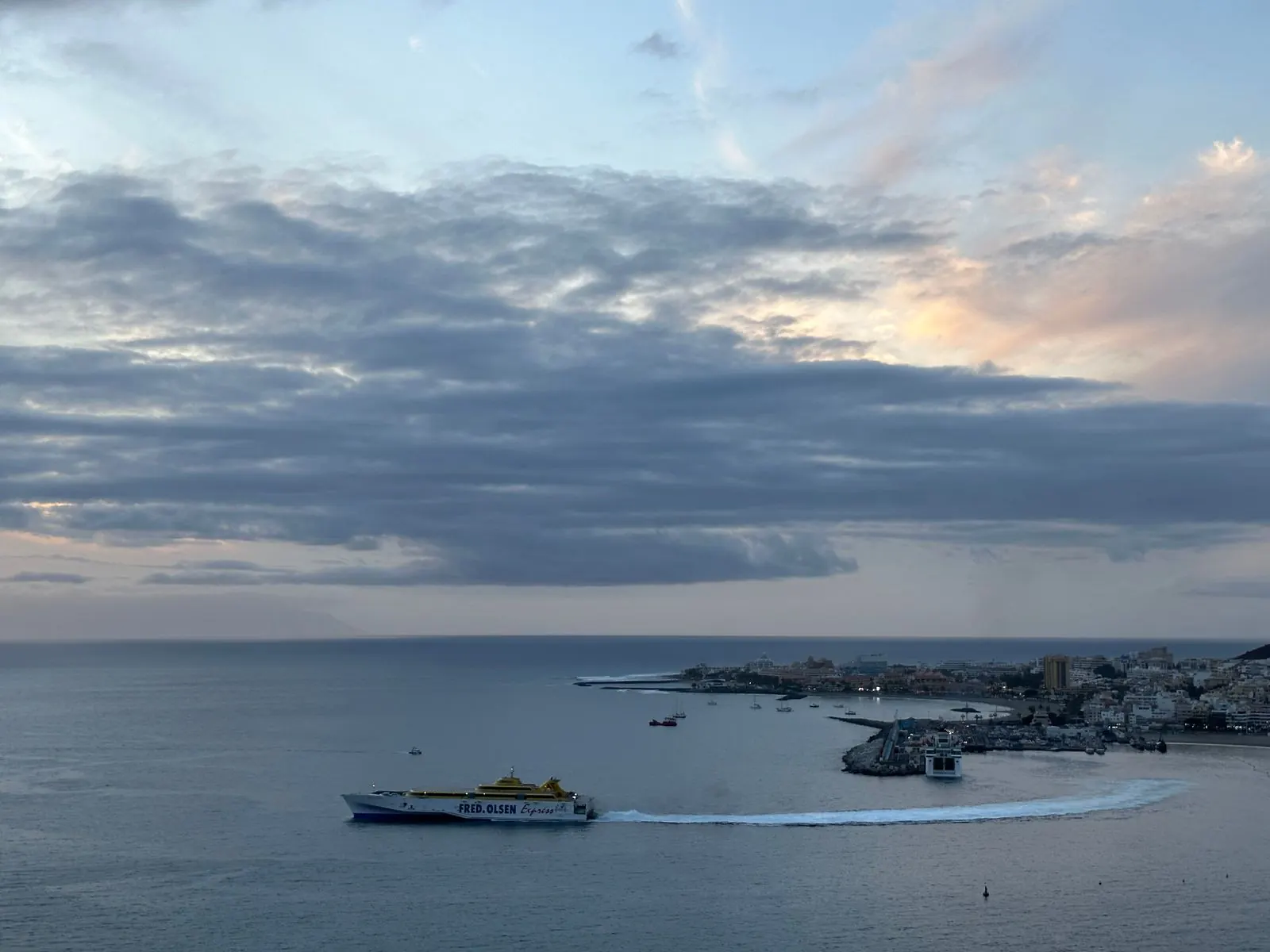 Fred. Olsen fast ferry leaving Los Cristianos harbour at dusk, with the town and breakwater on the right