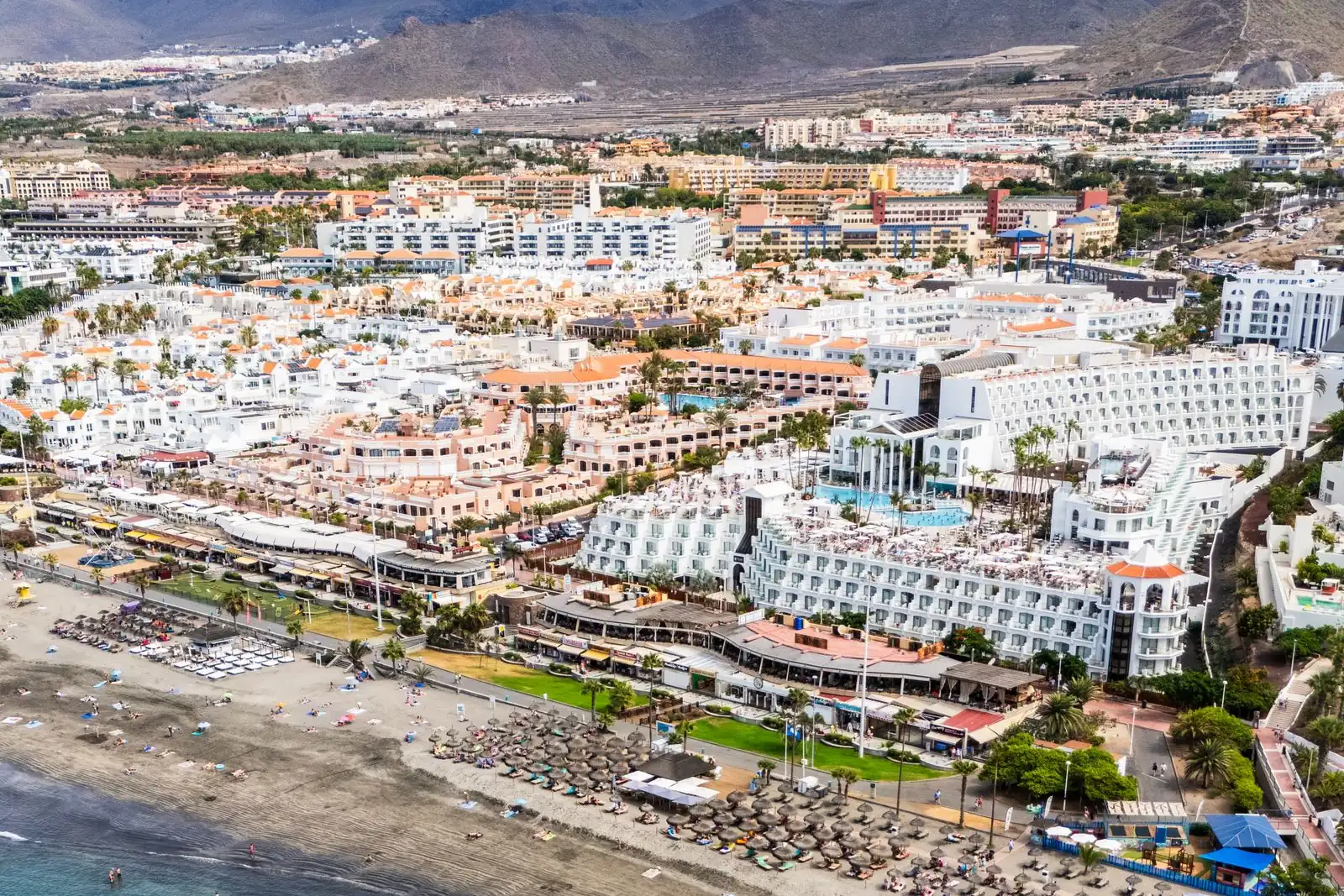 Aerial view of Playa de las Américas with hotels and apartments behind a grey-sand beach and mountains inland