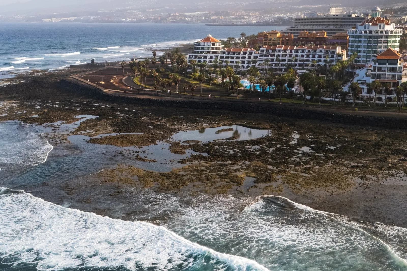 Waves breaking on the volcanic reef off the Playa de las Américas seafront, with the promenade and hotels behind