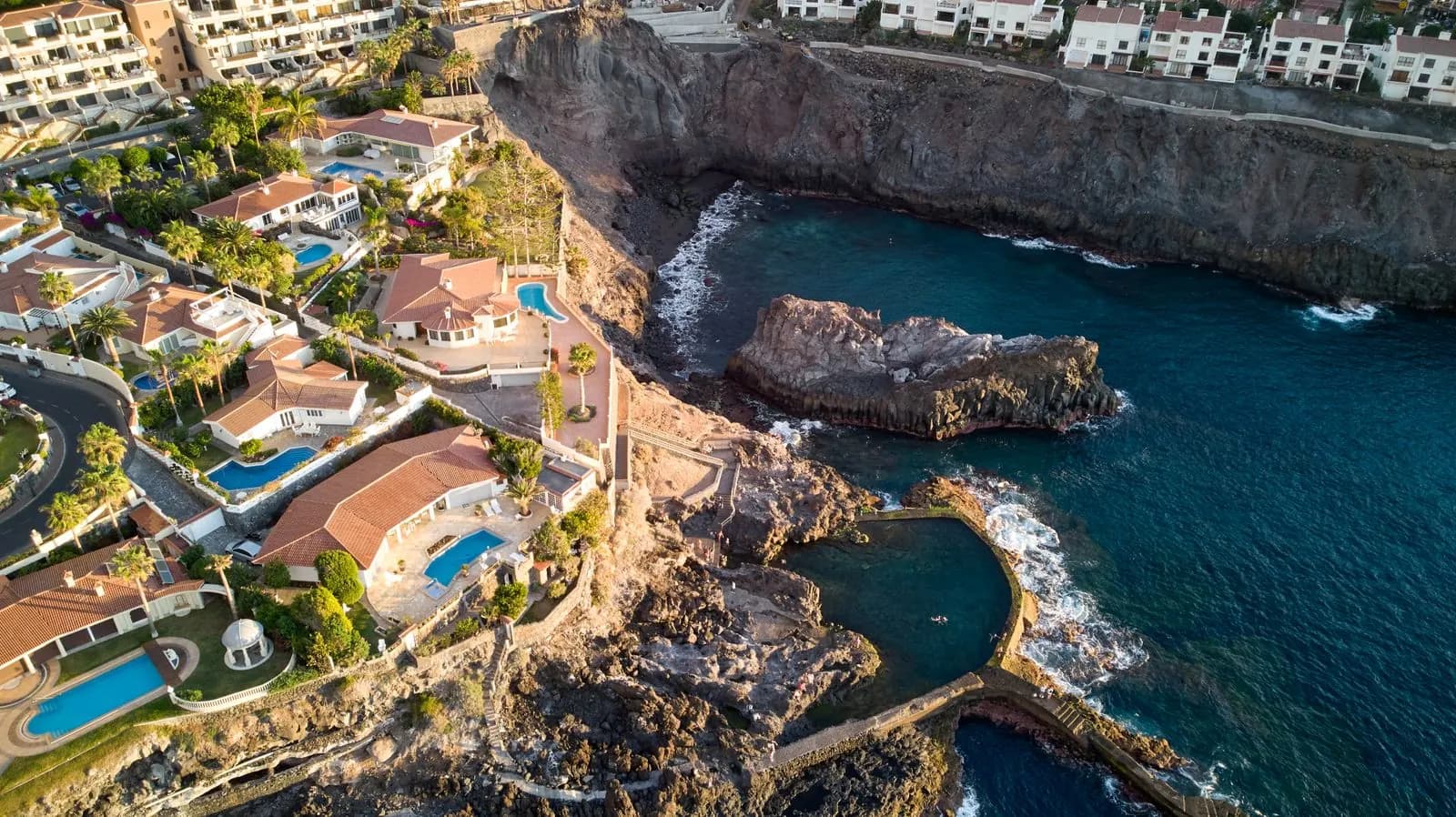 Aerial view of clifftop villas with private pools above a rocky cove and sea pool on Tenerife's south-west coast