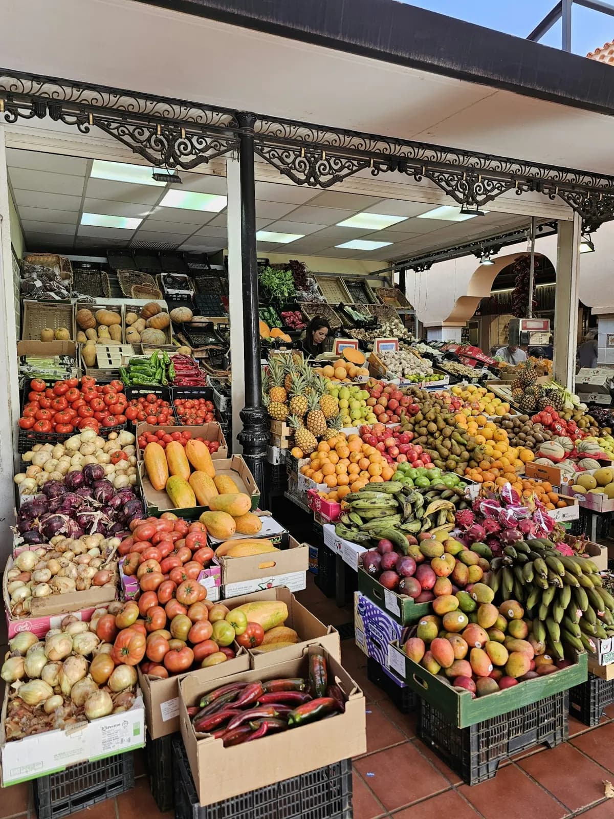 Bancarella di un mercato a Santa Cruz de Tenerife piena di pomodori, cipolle, papaie, ananas, manghi e banane sotto una tettoia in ferro battuto