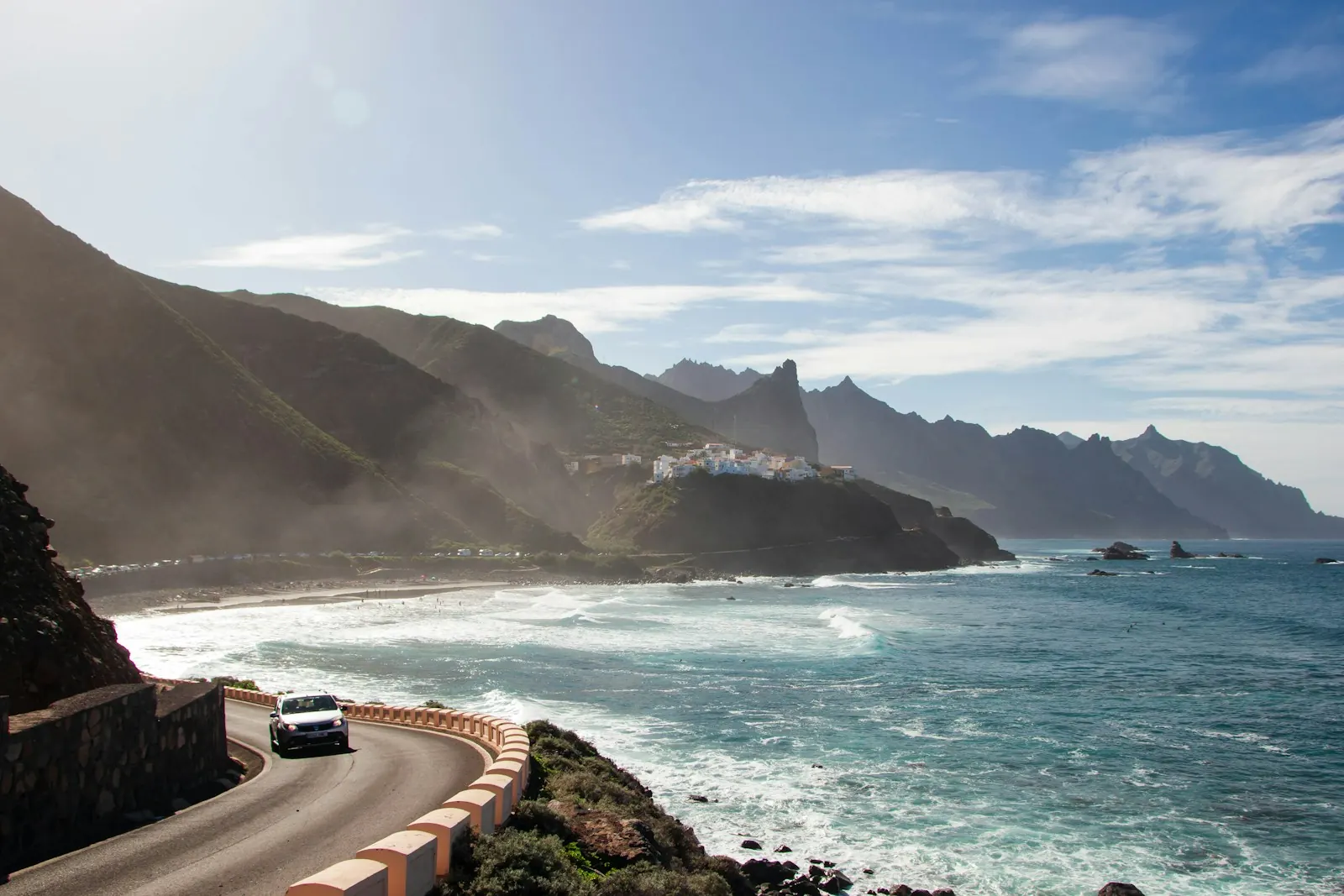 Auto su una strada costiera a curve nei monti di Anaga, nel nord-est di Tenerife, sopra le onde, una spiaggia di sabbia nera e un paesino sulla collina