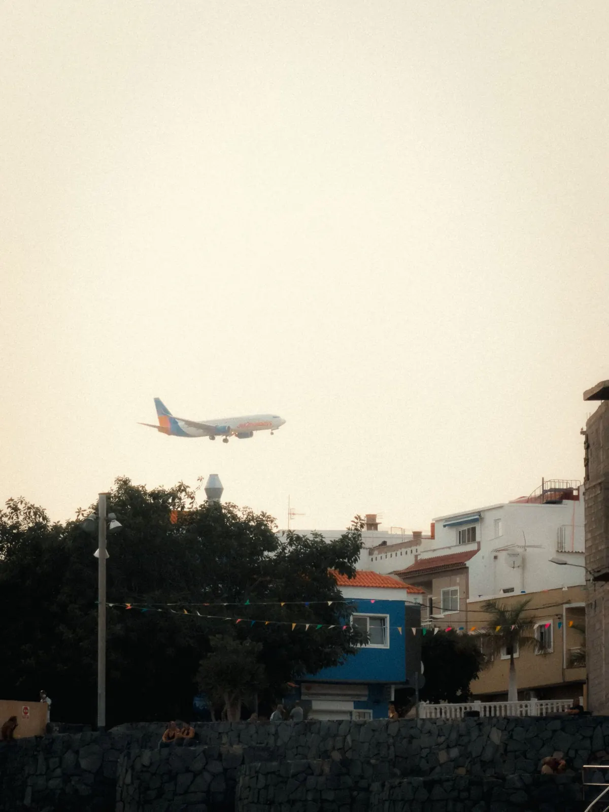 Airliner on final approach over houses and a volcanic stone wall in Tenerife at dusk
