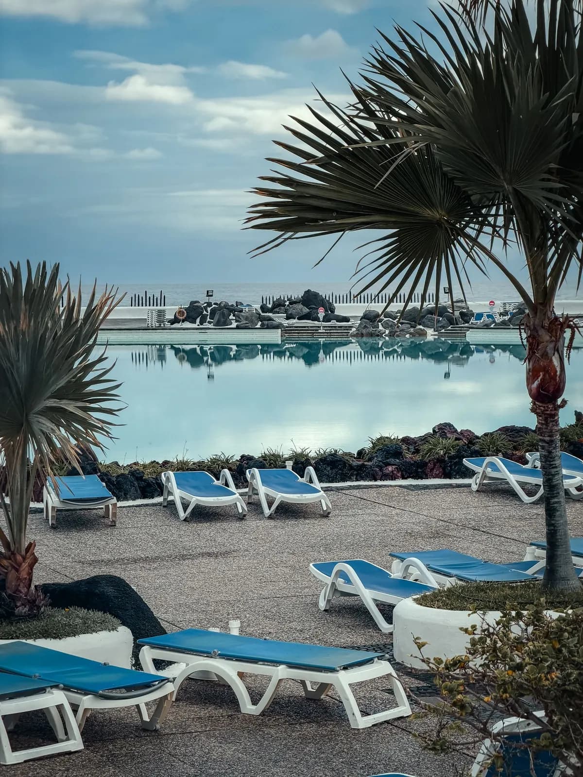 Lettini e palme accanto a una grande piscina con l'Atlantico sullo sfondo sotto un cielo nuvoloso a Puerto de la Cruz, nel nord di Tenerife