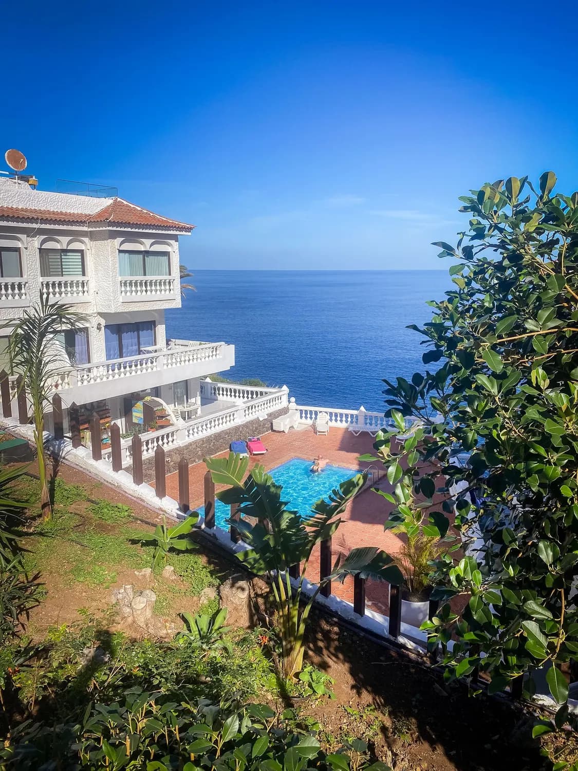 Villa con piscina privata su una terrazza sopra l'oceano a Tenerife, vista tra le piante del giardino in una giornata limpida