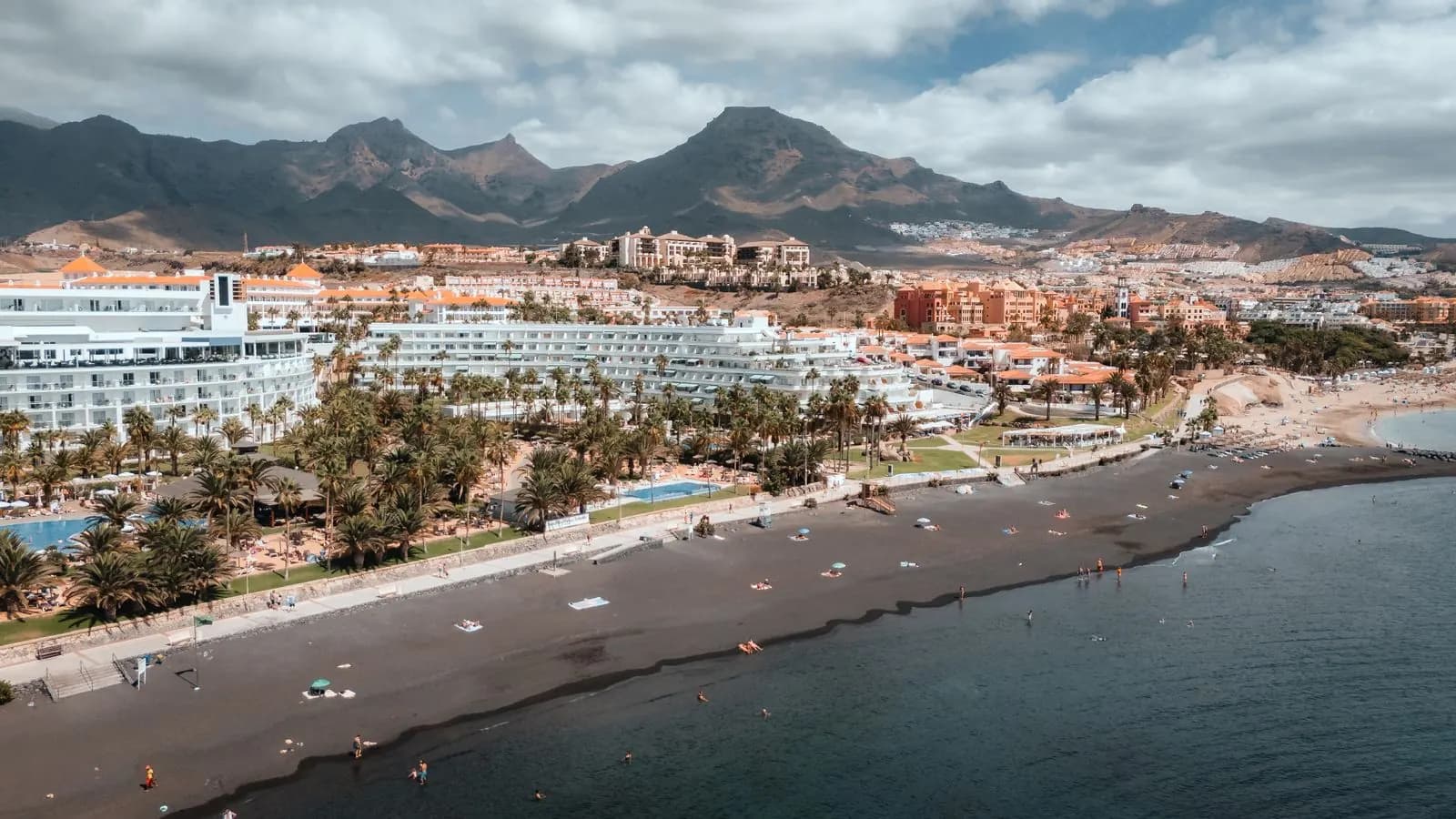 Hotel fronte mare, palme e lungomare sulla costa di Adeje, con ville e le montagne di Adeje sullo sfondo