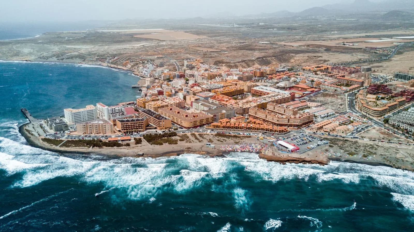 Aerial view of El Médano, with hotels and apartment blocks along the shore and flat coastal land stretching inland behind